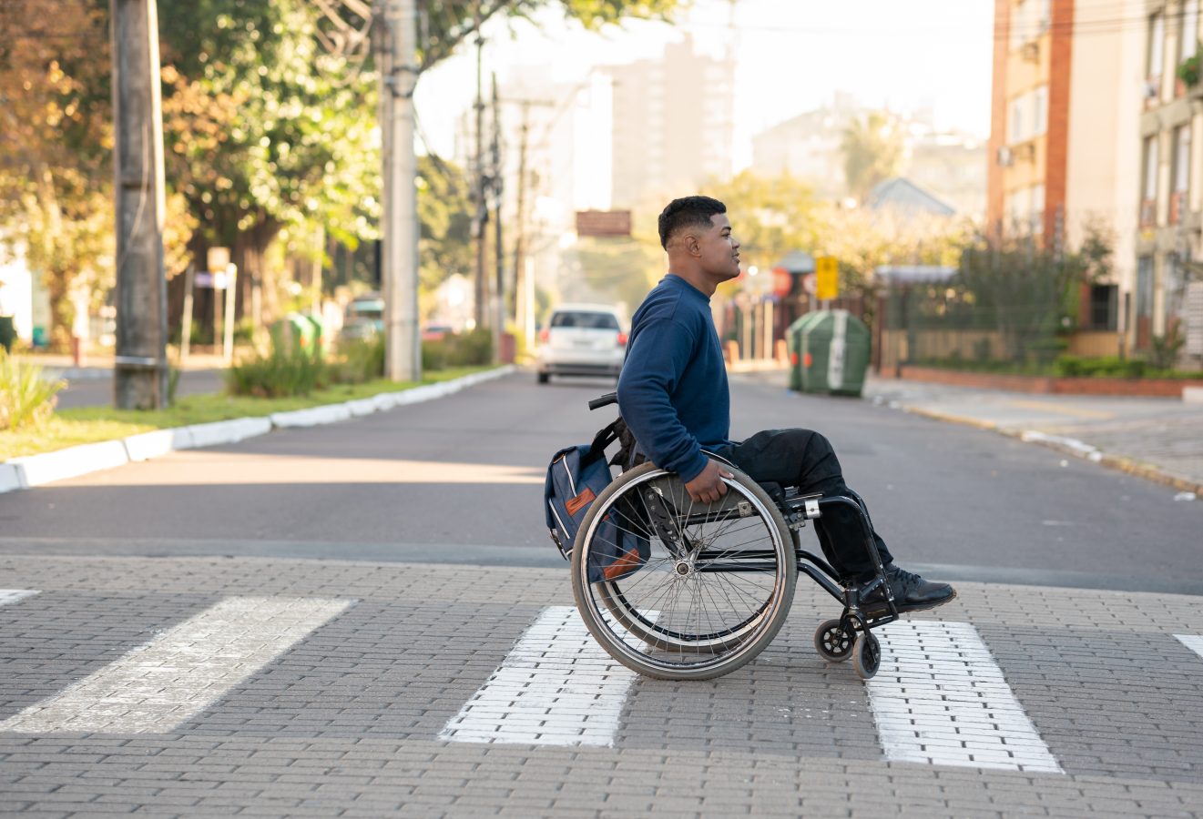 Young guy traveling in a city crosses the street on the sidewalk in his wheelchair.